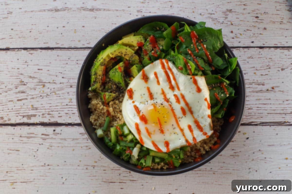 Avocado Breakfast Power Bowl 9 egg on top of quinoa and veggies drizzled with sriracha sauce and sprinkled with seasoning in a black bowl