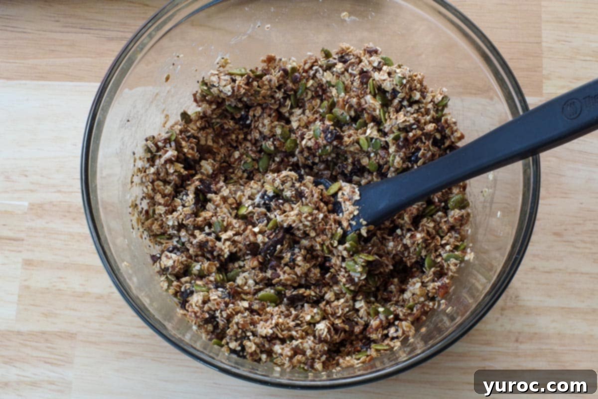 The melted liquid mixture has just been poured into the large glass bowl containing the dry ingredients, and a black silicone spatula is used to thoroughly combine everything.