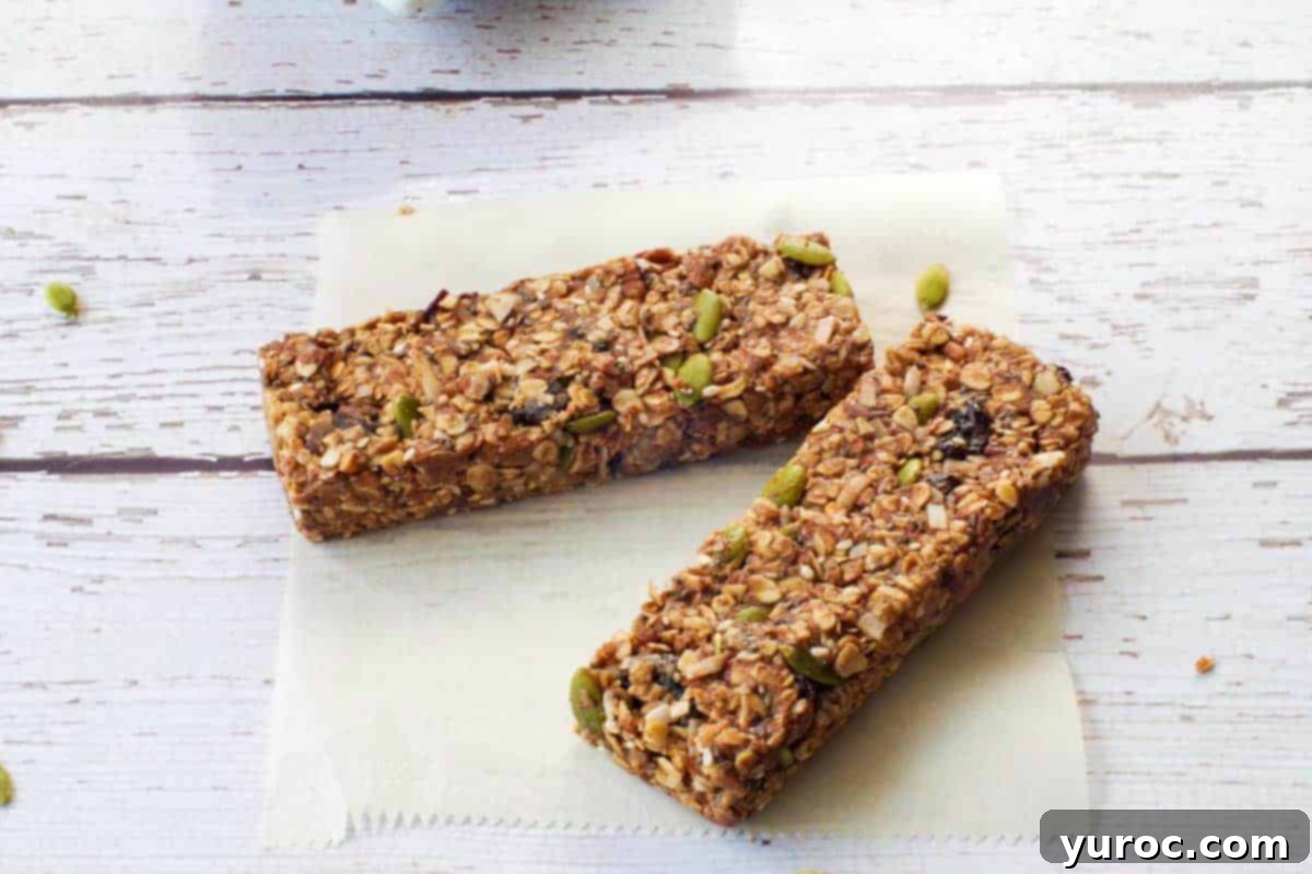 Two perfectly formed No Bake Almond Butter Granola Bars resting on a piece of rustic parchment paper, highlighting their delightful texture.