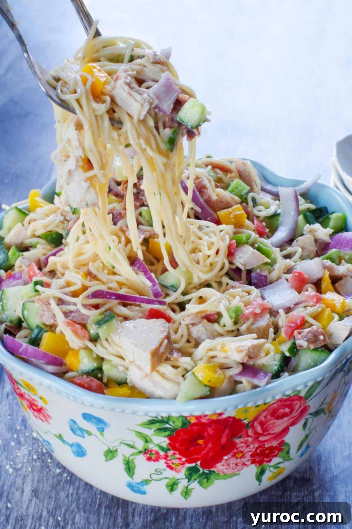 chicken bacon ranch pasta salad being lifted out of a flowered bowl with salad utensils
