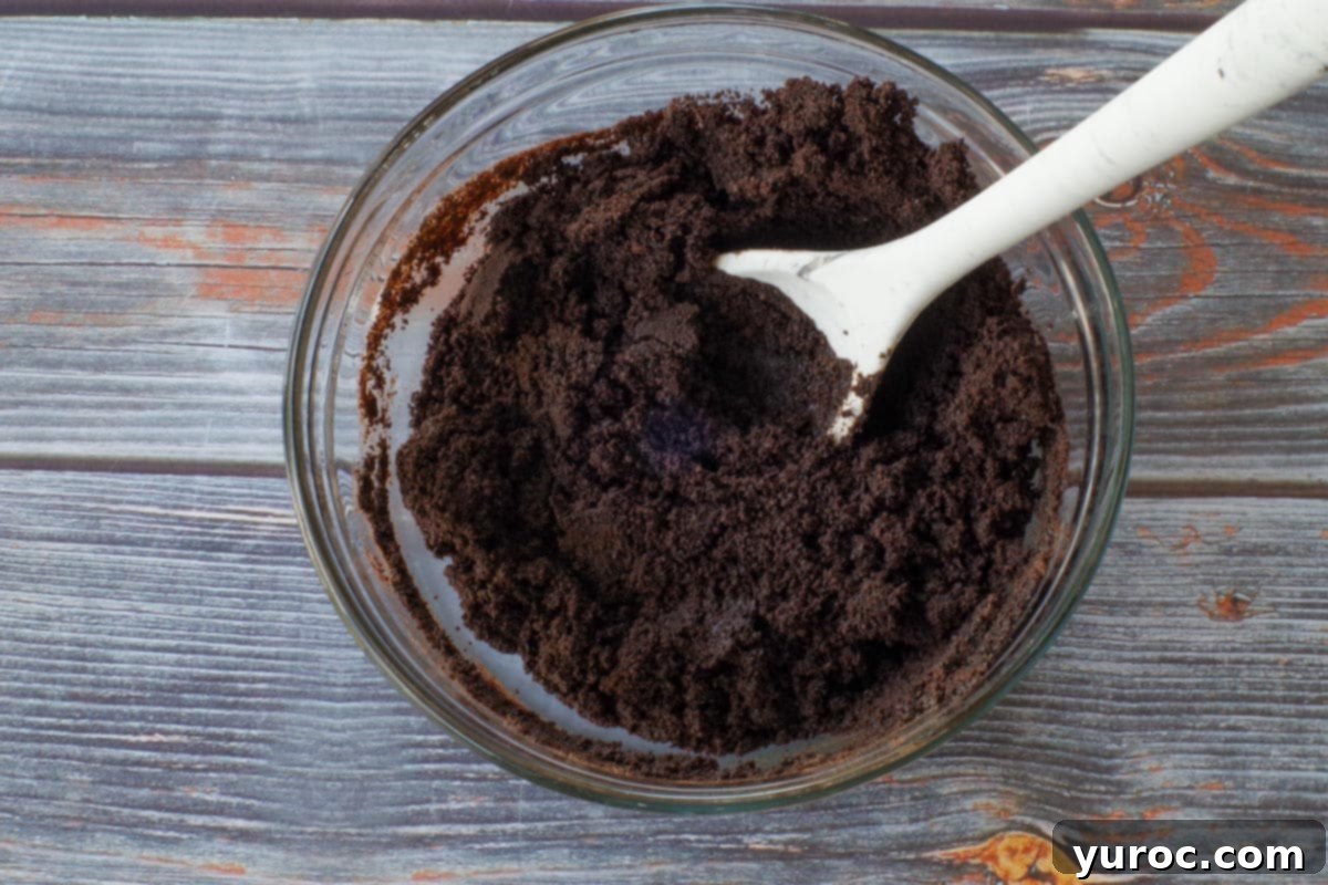 Chocolate crumbs and melted butter mixed in a glass bowl with spoon ( to form cheesecake bar base)