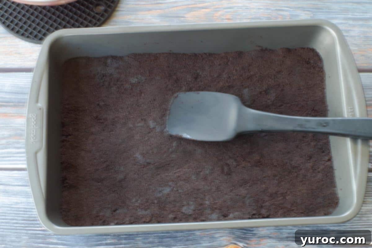 Chocolate mixture pressed into the bottom of a 9x13 pan to create base, with black spatula to flatten and taper edges