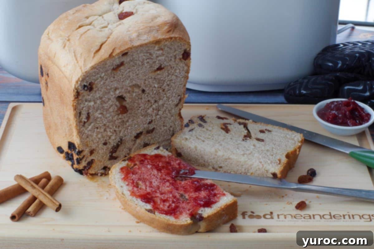 a slice of cinnamon raisin bread machine bread cut in half, with on side spread with jam, in front of a partial loaf of bread, on a cutting board