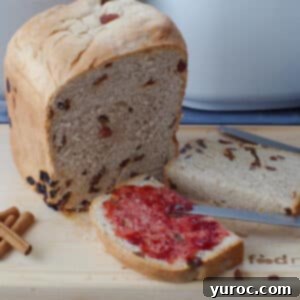 a slice of cinnamon raisin bread machine bread cut in half, with on side spread with jam, in front of a partial loaf of bread, on a cutting board