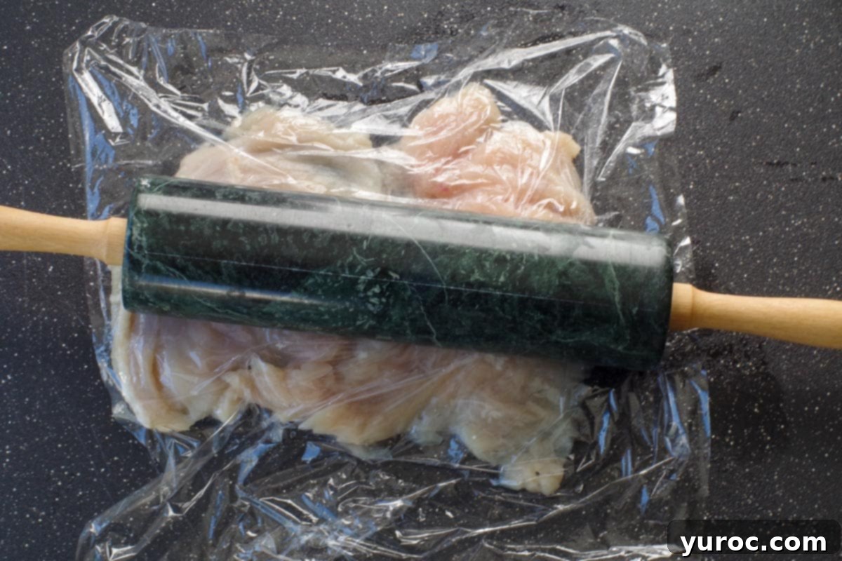 chicken breast being pounded down with rolling pin
