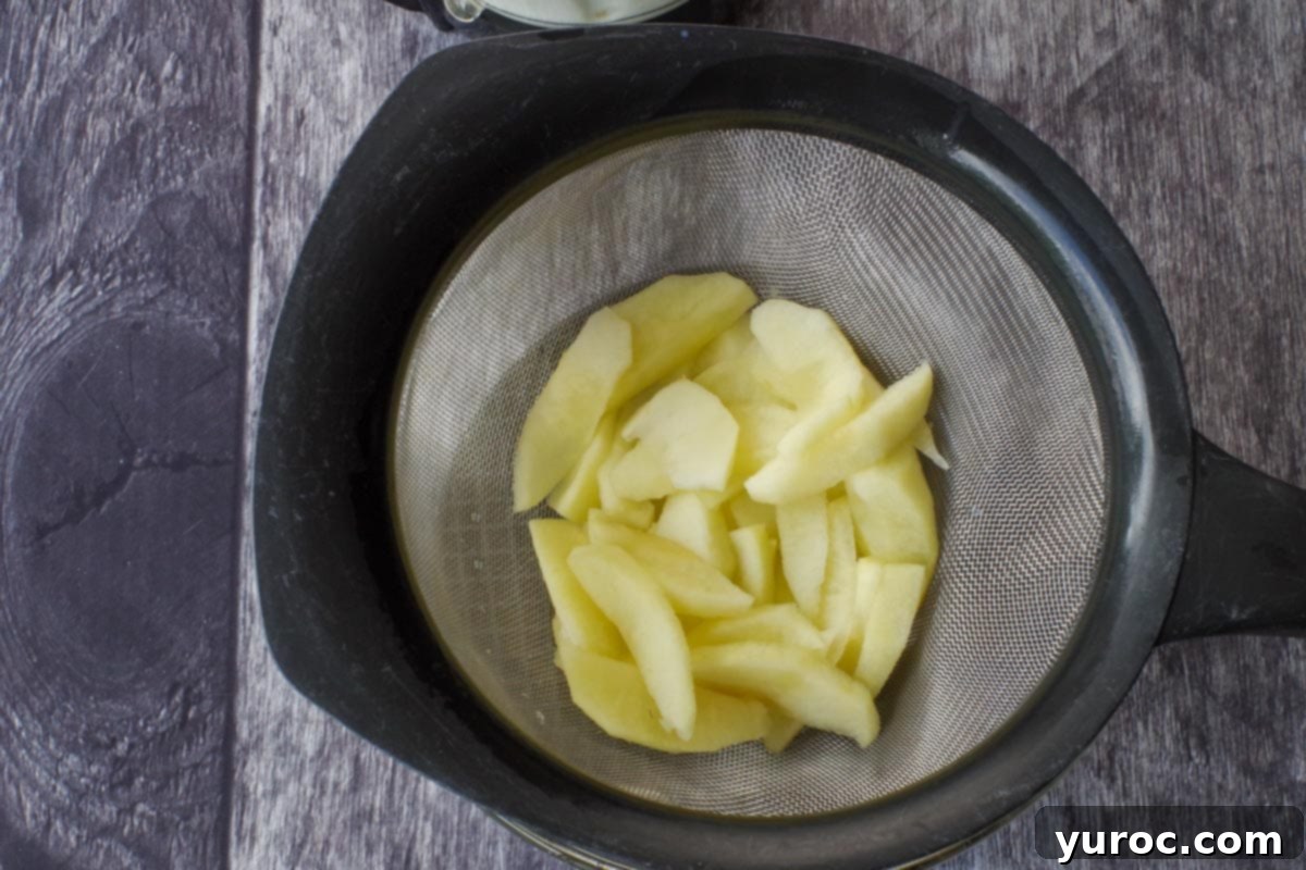Wholesome Apple Pie Spice Blend 5 Cooked, sliced apples draining through a sieve into a bowl to remove excess liquid.