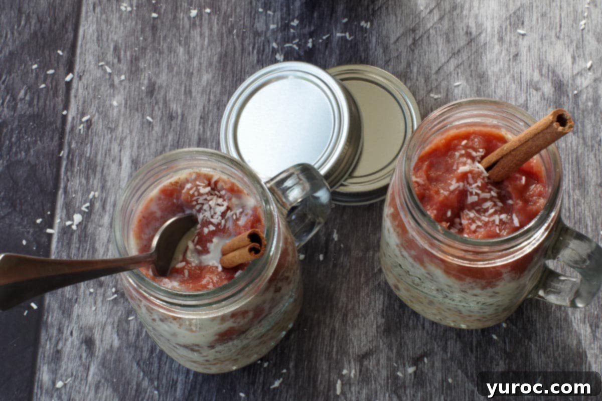 Two jars of rhubarb overnight oats, with vibrant rhubarb purée added, garnished with a sprinkle of coconut and a cinnamon stick, ready to be enjoyed.