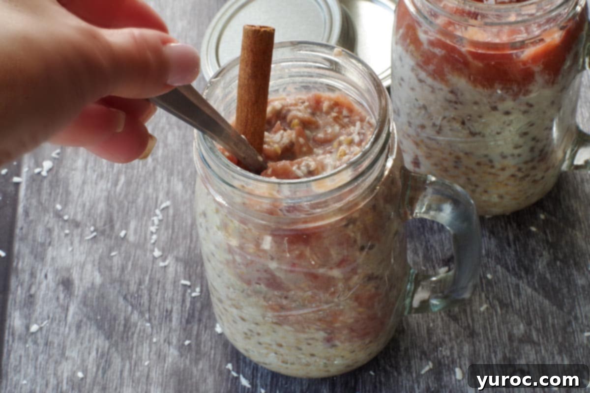 A hand stirring rhubarb overnight oats in a jar, blending the vibrant rhubarb purée with the creamy oat base.