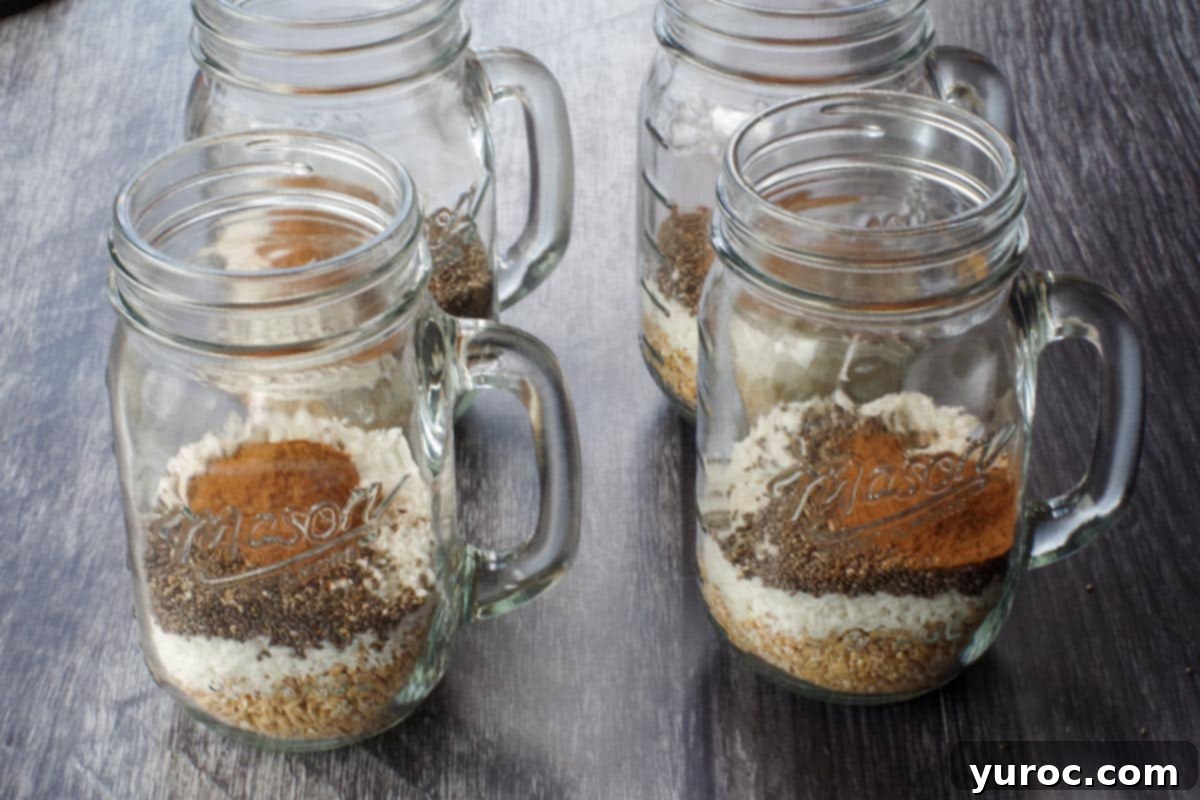 Four mason jars containing a dry mixture of cinnamon, oats, chia seeds, and unsweetened coconut, ready for liquids to be added.