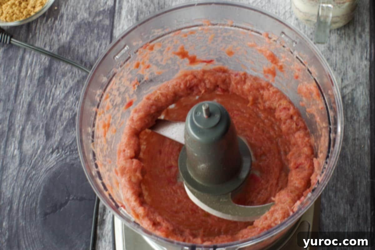 Cooked rhubarb being pureed to a smooth consistency in a food processor, ready for sweetening.