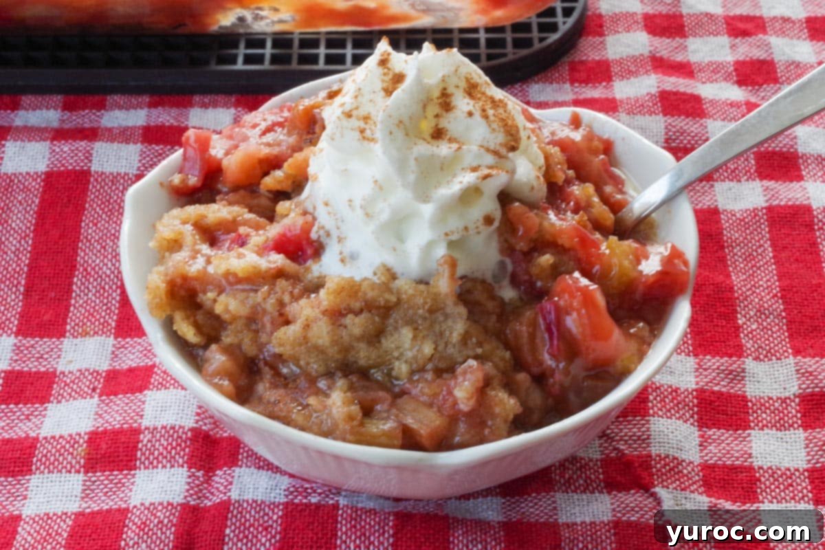 A single serving of rhubarb crumble, elegantly presented in a white petal dish, generously topped with whipped cream and a spoon beside it, inviting a taste.