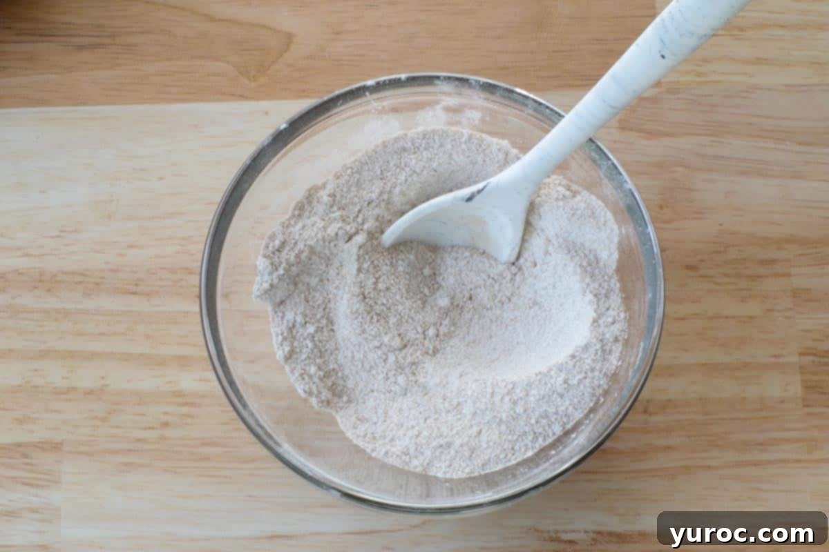Dry ingredients for the crumble topping, including flour, sugars, and cinnamon, perfectly mixed together in a glass bowl with a silicone spoon.