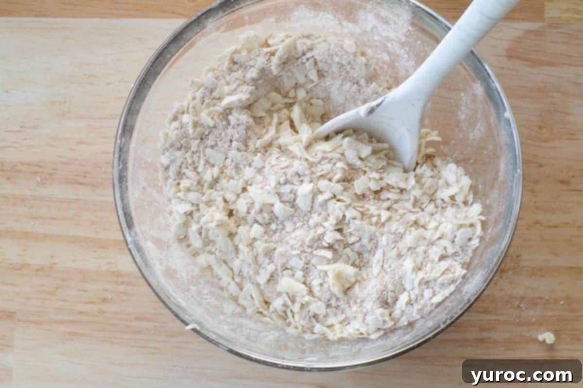 Grated cold butter evenly mixed into the dry crumble topping ingredients in a glass bowl, creating a perfect crumbly texture.