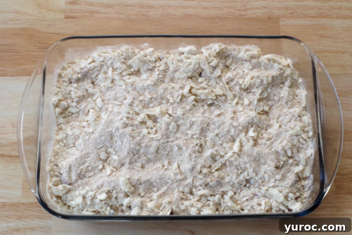 The prepared crumble topping spread evenly over the rhubarb and whipped cream layers in the glass baking pan, ready for baking.