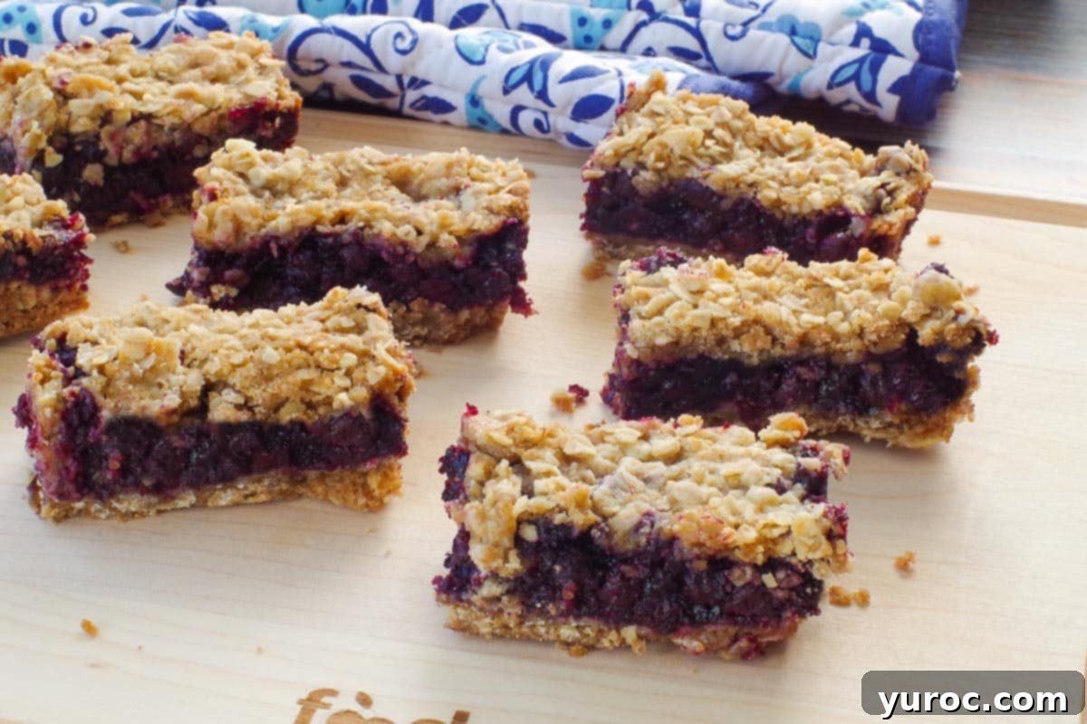 Saskatoon Berry Bliss Bars 14 8 smaller Saskatoon bars on a wooden cutting board with blue and white patterned oven mitts in the background