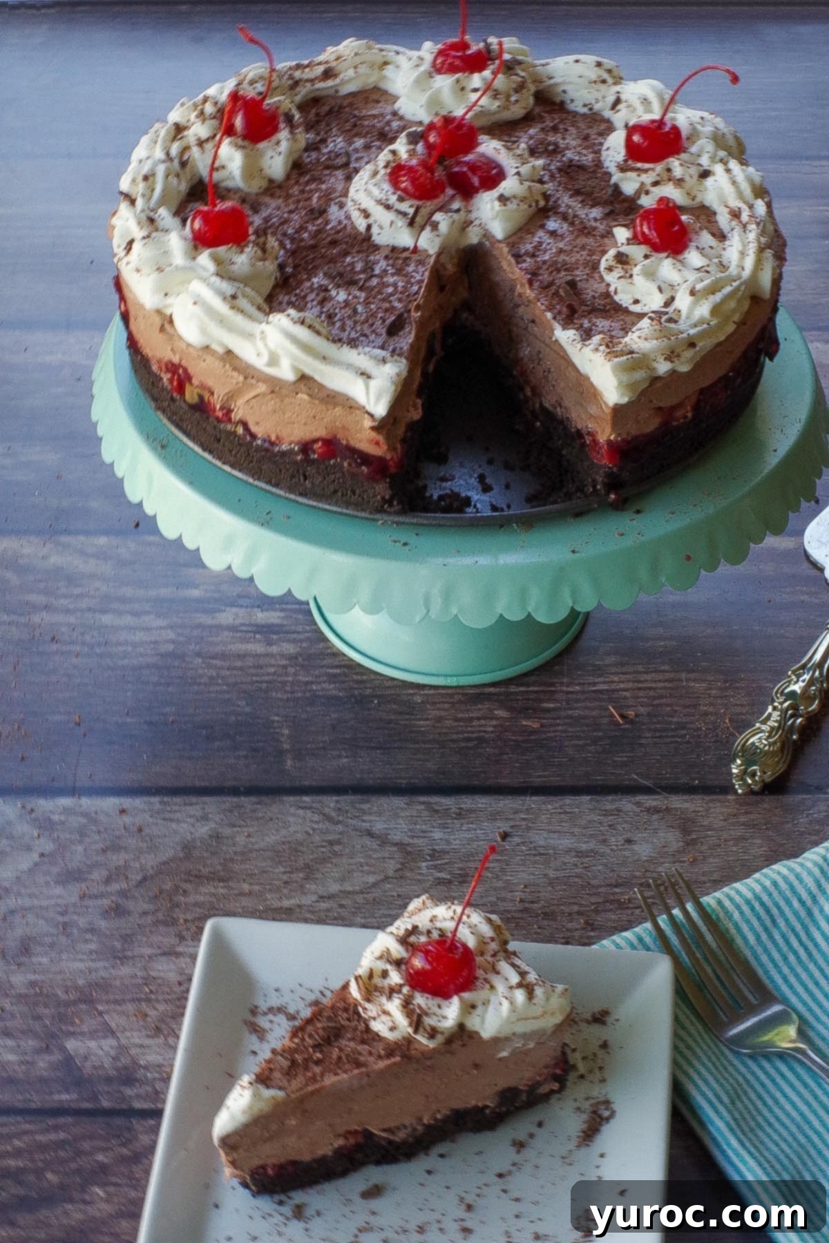 A whole No-Bake Black Forest Cheesecake with one slice removed, elegantly displayed on a turquoise cake stand. A single slice is also shown on a white plate in front.
