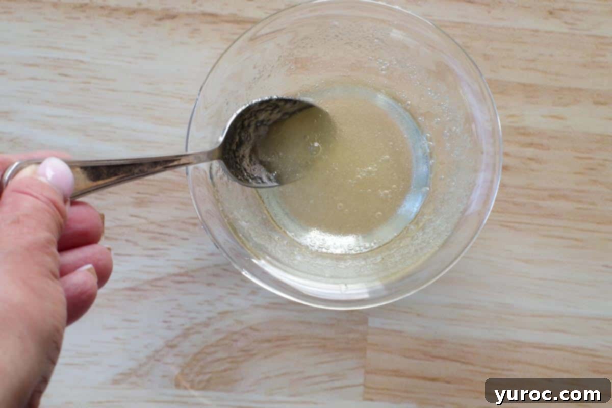 Gelatin powder being stirred into hot water in a small glass bowl with a spoon until fully dissolved.