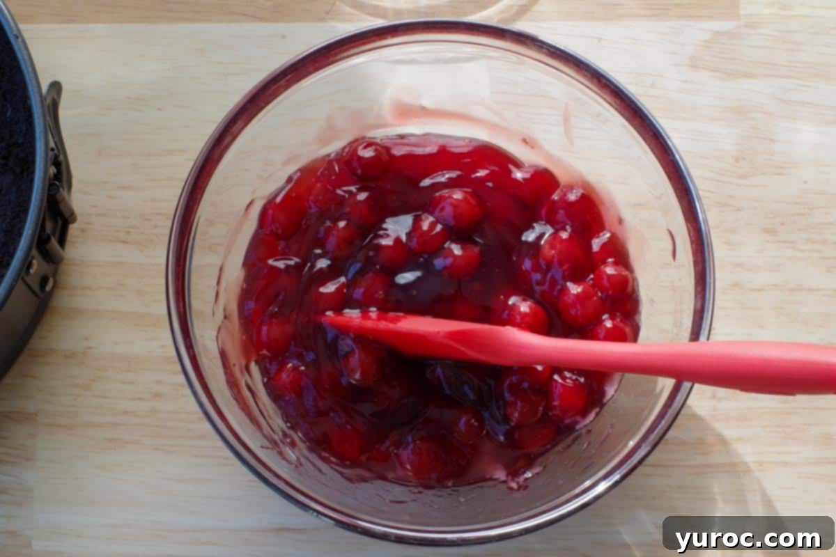 Cherry pie filling mixed with dissolved gelatin and almond extract in a glass bowl, ready for the cheesecake.