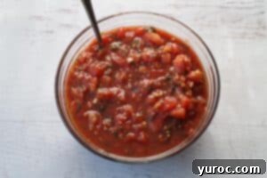 bruschetta ingredients mixed together in glass bowl , with a spoon