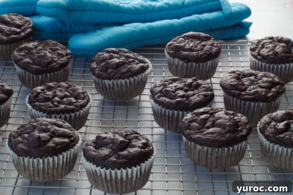 Chocolate Weight Watchers zucchini muffins on a wire cooling rack with a blue oven mitt in the background