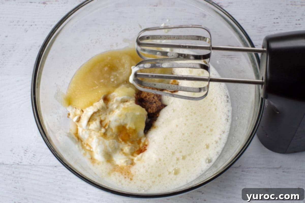 Greek yogurt, unsweetened applesauce, vanilla, and brown sugar mixed with eggs in a large glass bowl