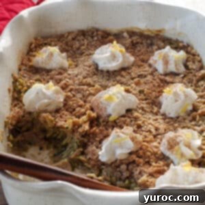 A top-down view of a round white baking dish filled with golden-brown zucchini crisp, dotted with peaks of whipped cream, invitingly presented.