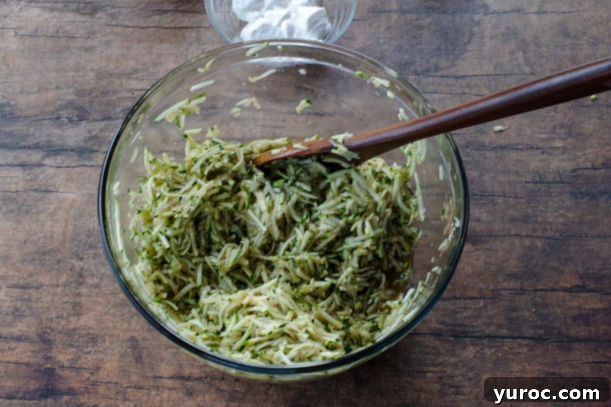 A close-up shot of shredded zucchini thoroughly mixed with brown sugar, cinnamon, and other liquid ingredients in a glass bowl, showcasing the consistency of the filling.