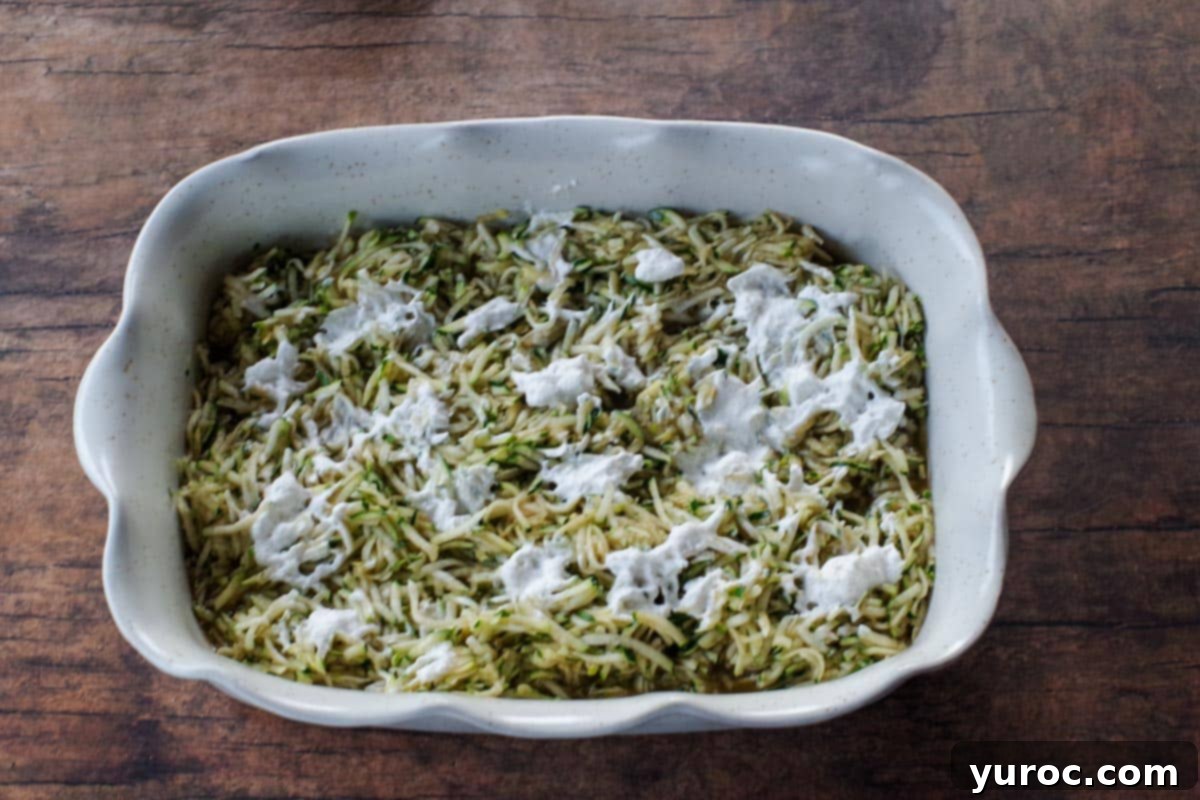 The mixed zucchini filling poured into a white ceramic baking dish, with small dollops of spray whipped cream dotted across the surface.
