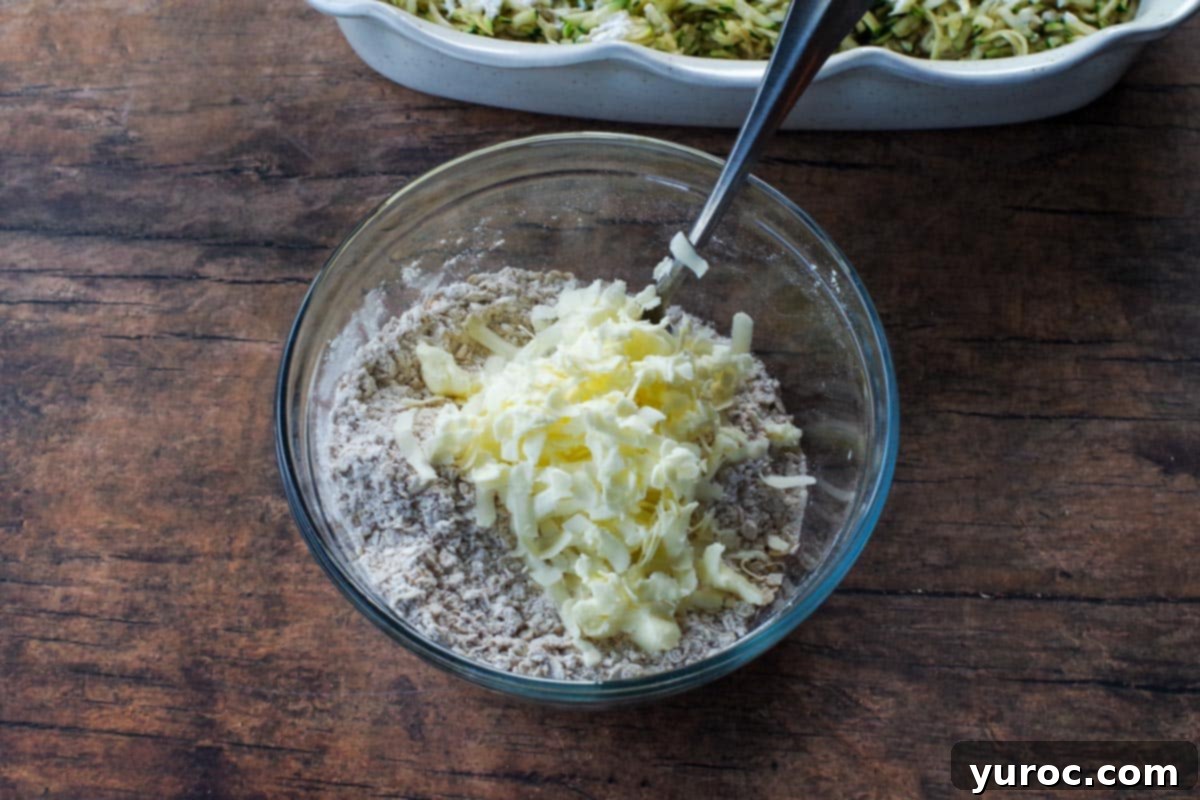 A glass bowl containing oats, flour, and brown sugar, with cold butter pieces cut into the mixture, beginning to form coarse crumbs for the crisp topping.