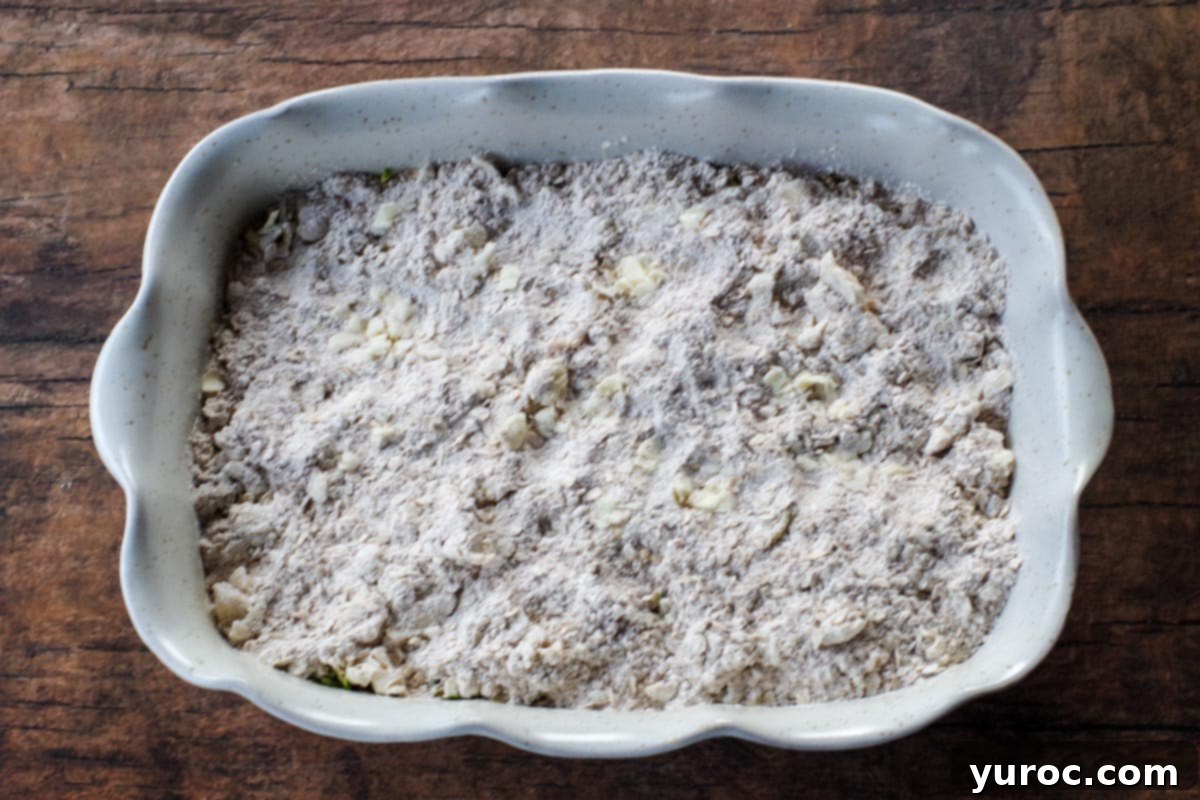 The baking dish, now with the prepared oat and flour crumb topping evenly sprinkled over the zucchini mixture, ready for baking.