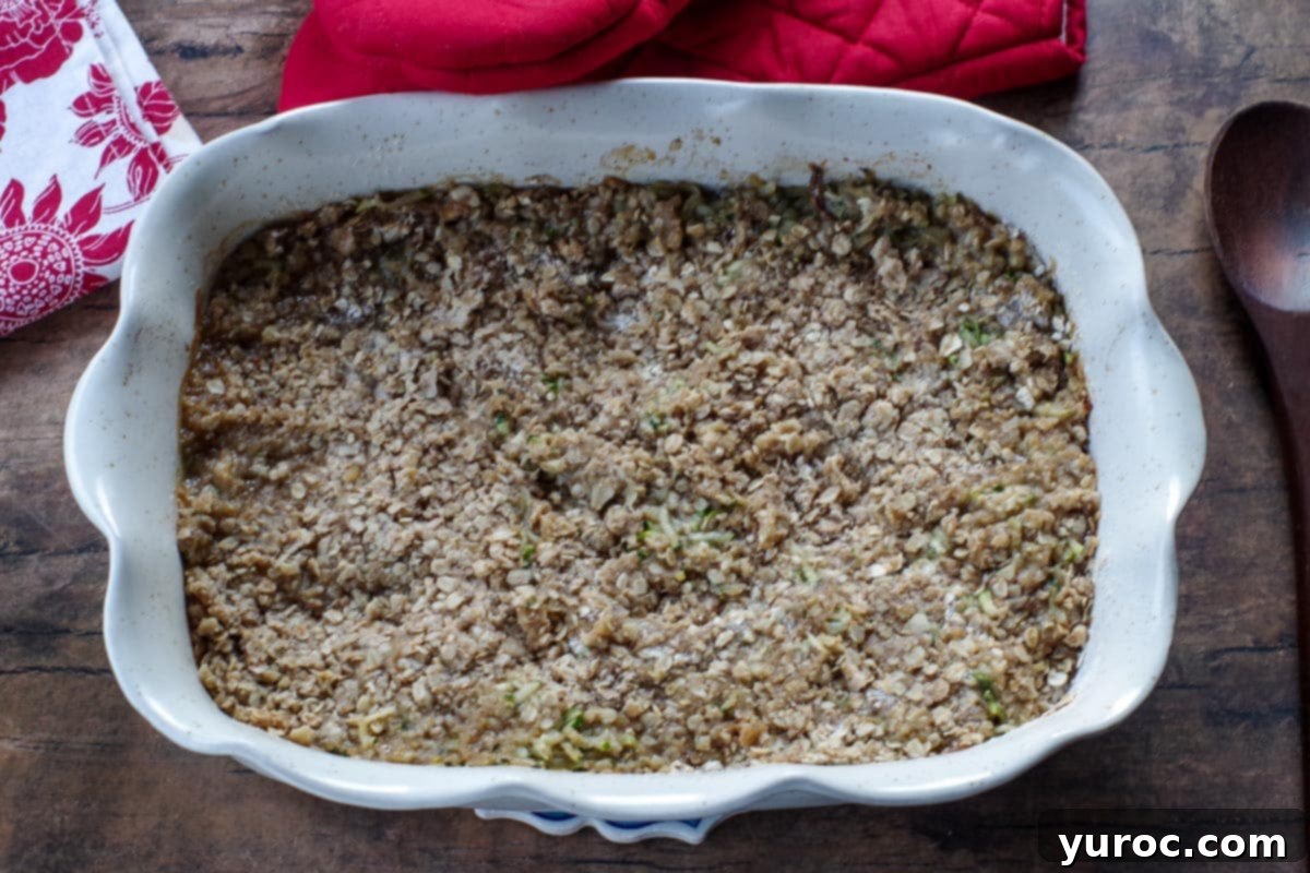 The baked zucchini crisp in a white ceramic baking dish, golden brown and bubbly, indicating it's perfectly cooked and ready to serve.