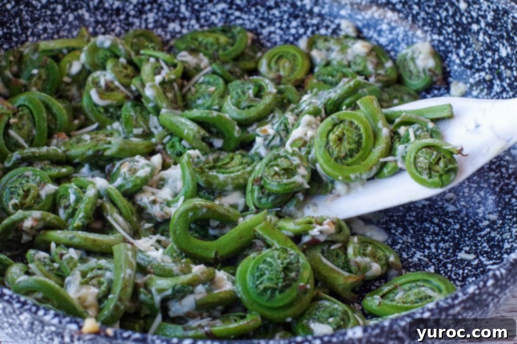 Cheesy Sauteed fiddleheads in a pan with a white spatula