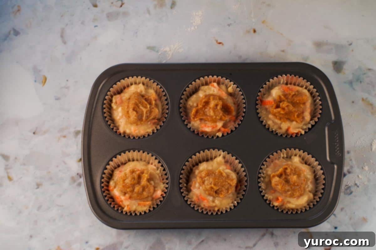 Glazed Carrot Cake Doughnut Muffins 12 A teaspoonful of jam mascarpone filling being dropped onto the muffin batter in each cup.