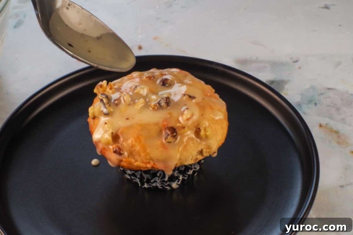 Glazed Carrot Cake Doughnut Muffins 17 Orange mocha glaze being spooned onto a carrot cake doughnut muffin resting on a black plate.