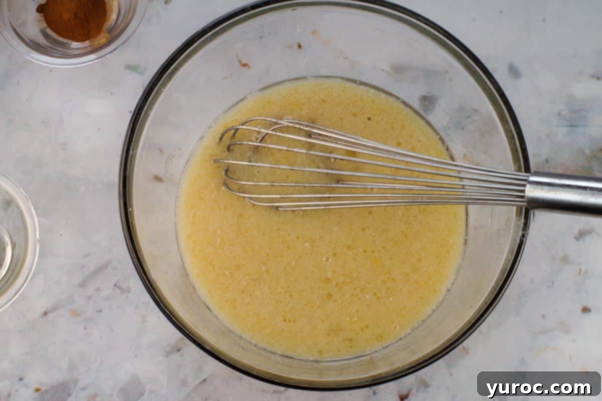 Glazed Carrot Cake Doughnut Muffins 6 Wet ingredients for muffins whisked together in a clear glass bowl with a metal whisk.