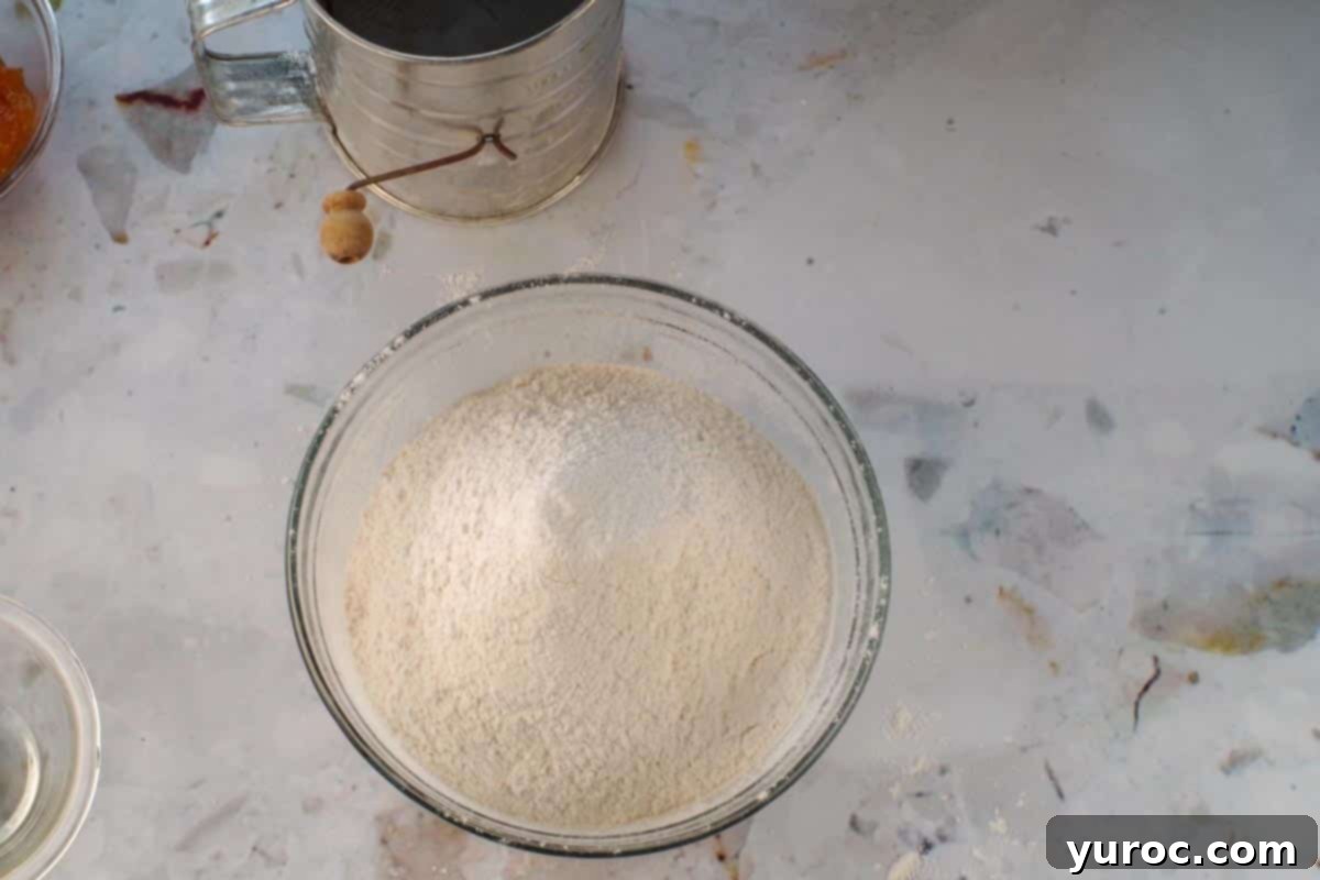 Glazed Carrot Cake Doughnut Muffins 8 Dry ingredients for muffins, including flour, baking powder, salt, and cinnamon, sifted together in a separate glass bowl.