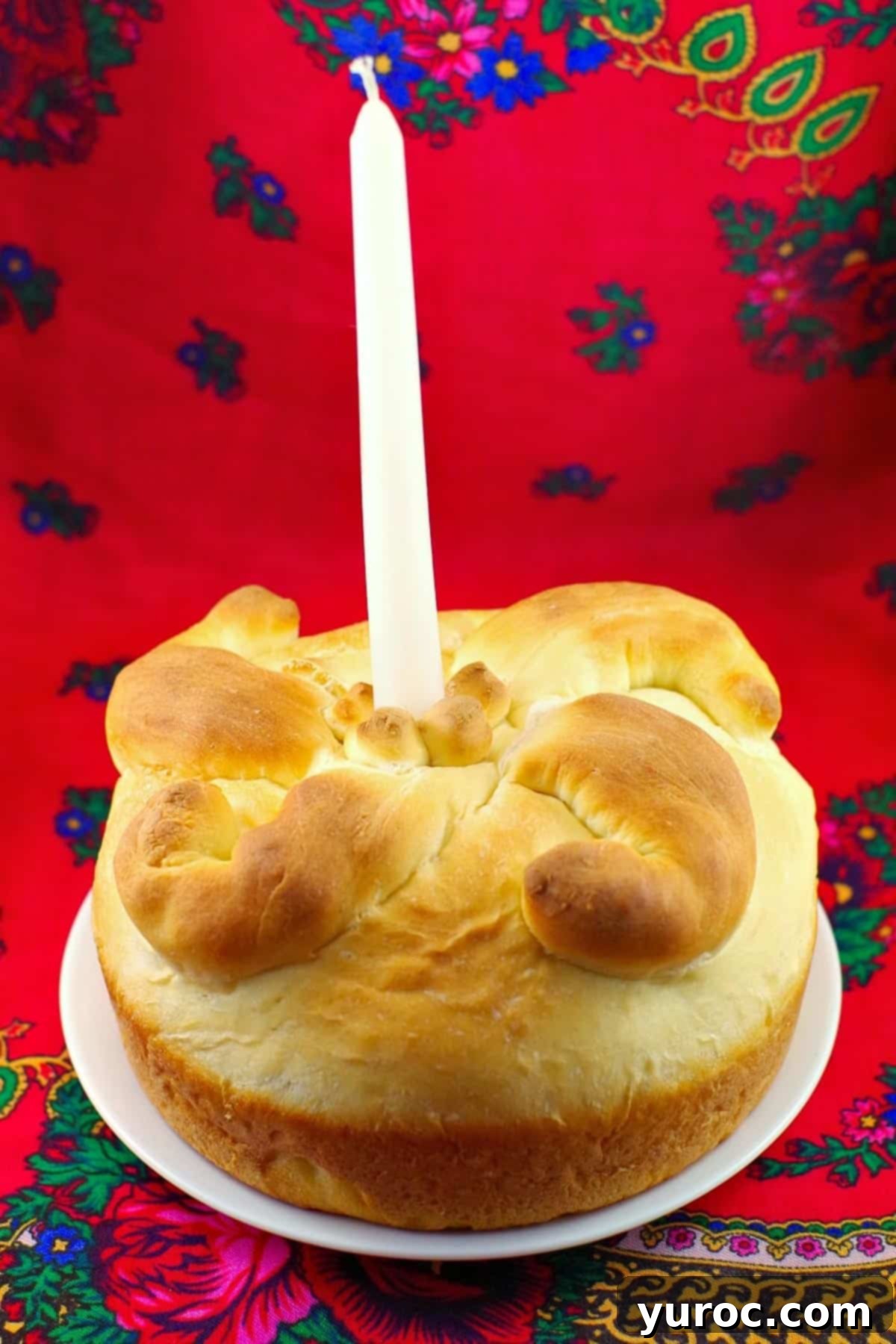 Bread Machine Paska with a white candle in the middle of it on a white plate, symbolizing Easter tradition.