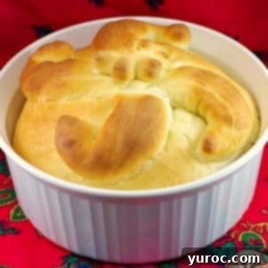 A beautifully baked Paska bread made in a bread machine, set in a round white casserole dish on a red patterned surface.