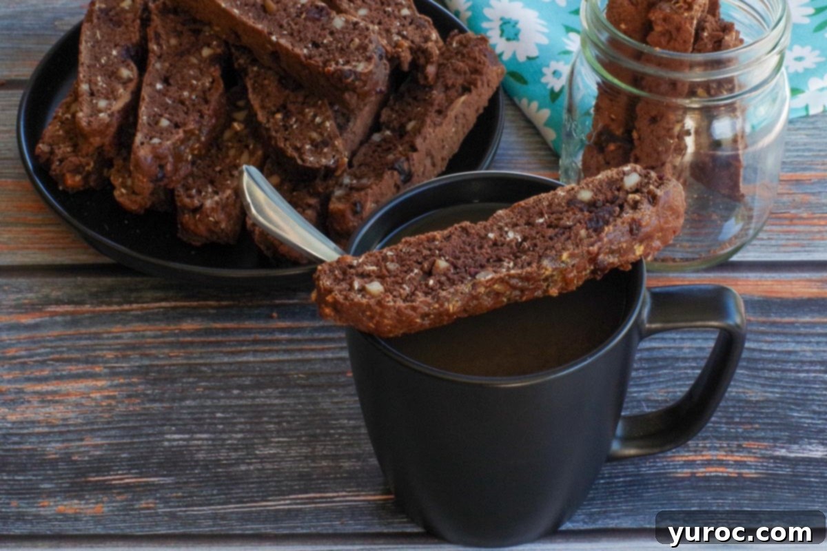 zucchini biscotti resting on top of a black coffee mug with a plate of more biscotti and a jar in the background