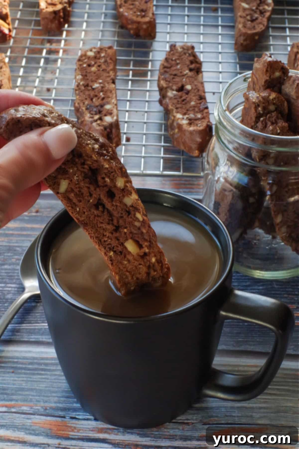 Zucchini Biscotti being dipped into a cup of coffee, with more zucchini on a wire rack in the background