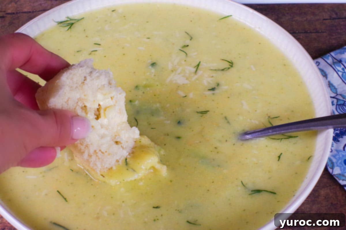 Wholesome Zucchini Potato Dill Soup 12 A freshly buttered Granny bun being dipped into a inviting bowl of warm Zucchini Potato Soup, highlighting the perfect pairing.