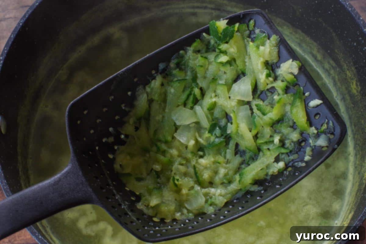 Wholesome Zucchini Potato Dill Soup 5 Cooked vegetables, including zucchini, onion, and garlic, being carefully strained from the simmering broth using a fine mesh strainer spoon.