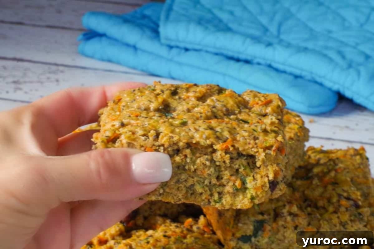A hand holding up a single healthy zucchini bar, showing its moist texture and rich ingredients.