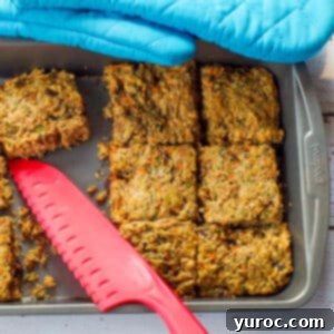 Freshly baked zucchini bars, perfectly cut in a pan, with a few slices already enjoyed, and a red silicone knife resting beside them.