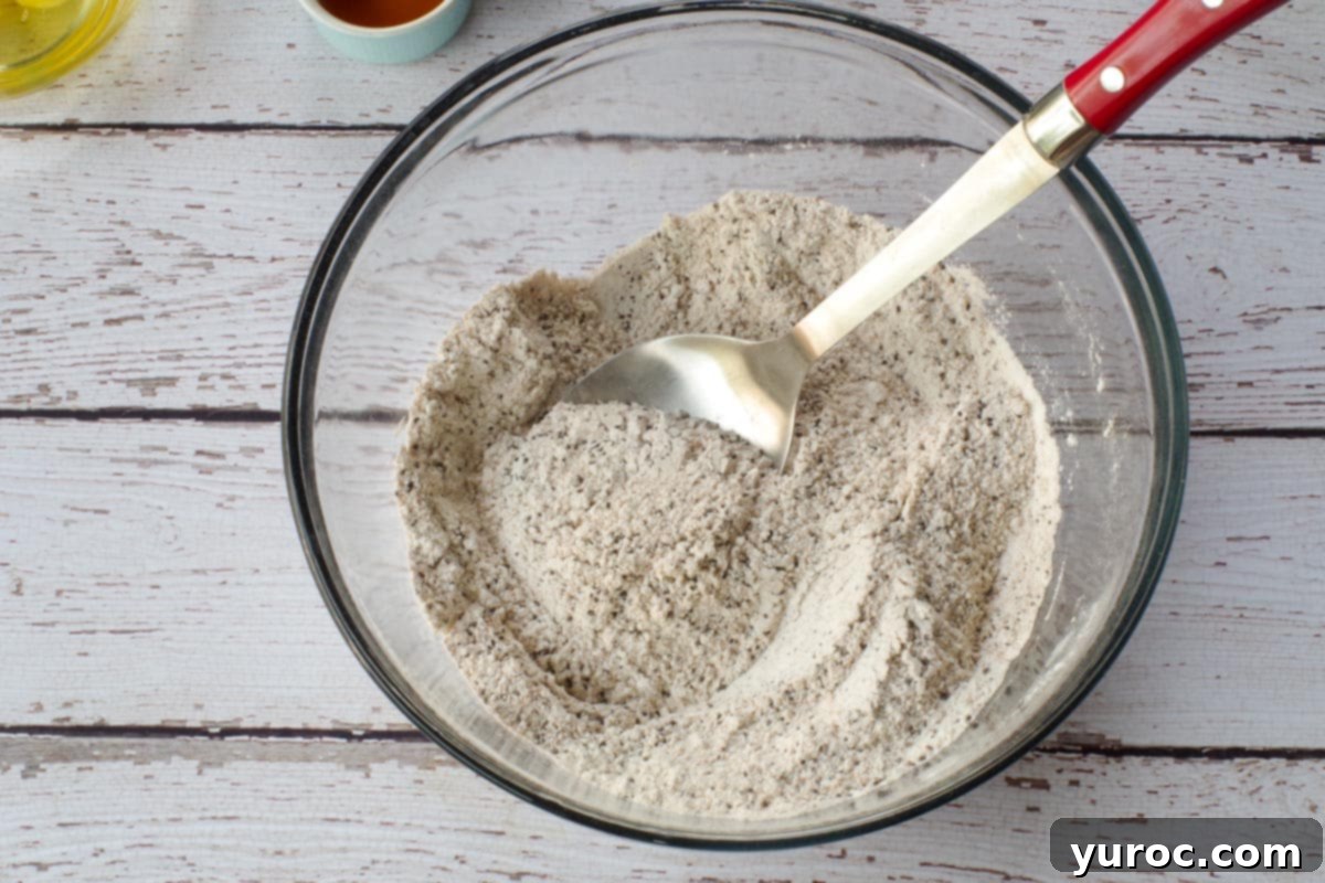 Dry ingredients for zucchini bars, including flours, spices, and sugar, mixed in a large glass bowl with a metal spoon.