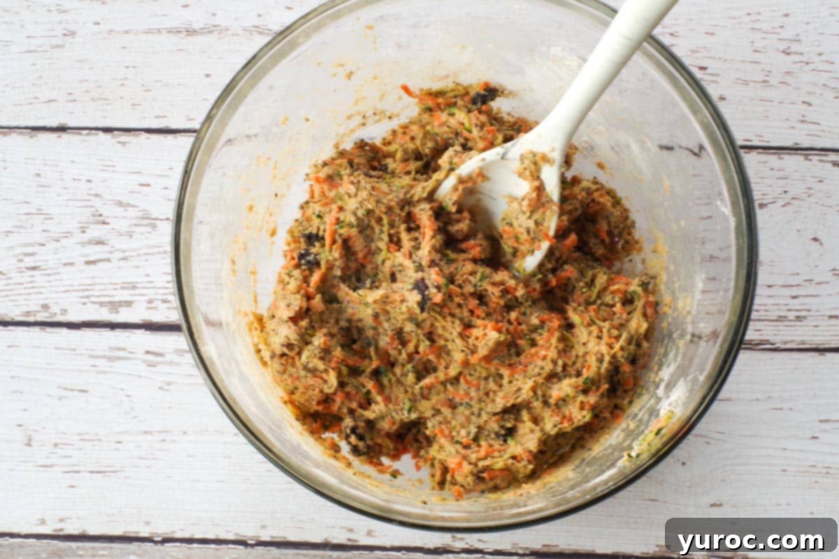 The combined wet and dry ingredients for zucchini bars, mixed to a consistent batter in a glass bowl with a silicone spoon.