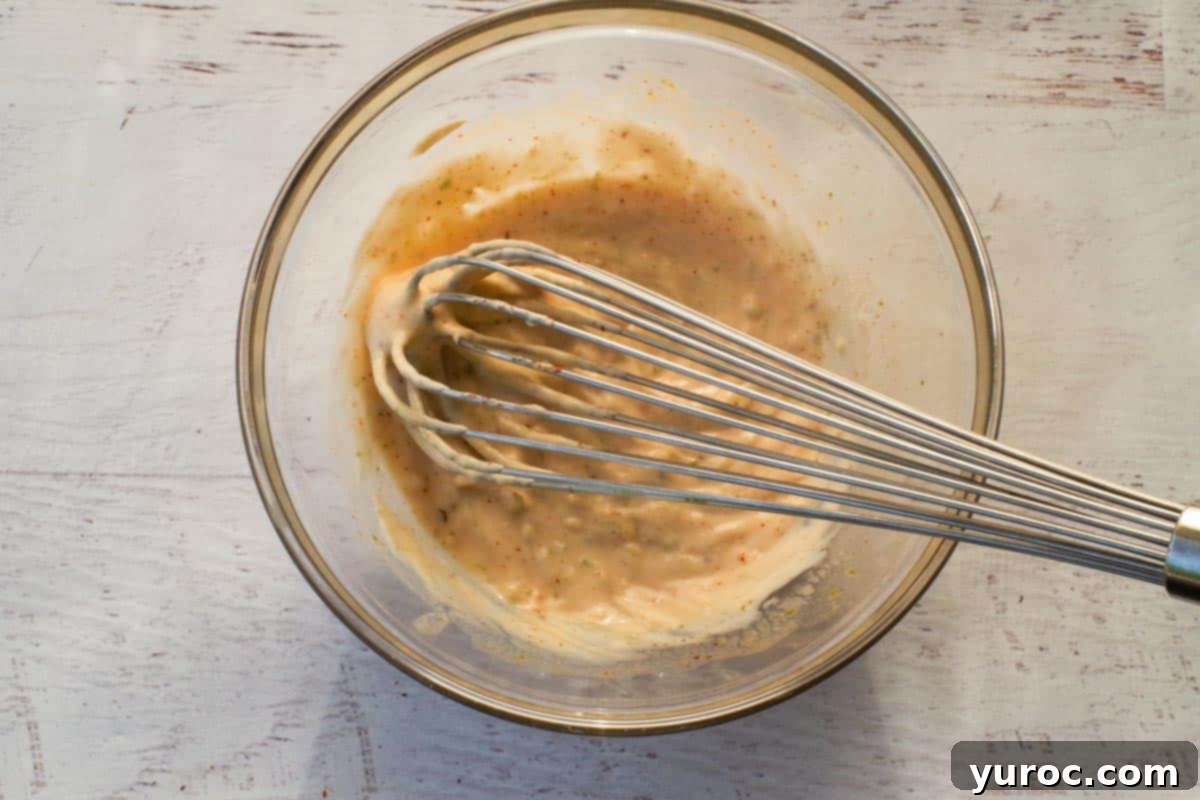Mexican Street Corn pasta salad dressing in a glass bowl, being mixed with a whisk