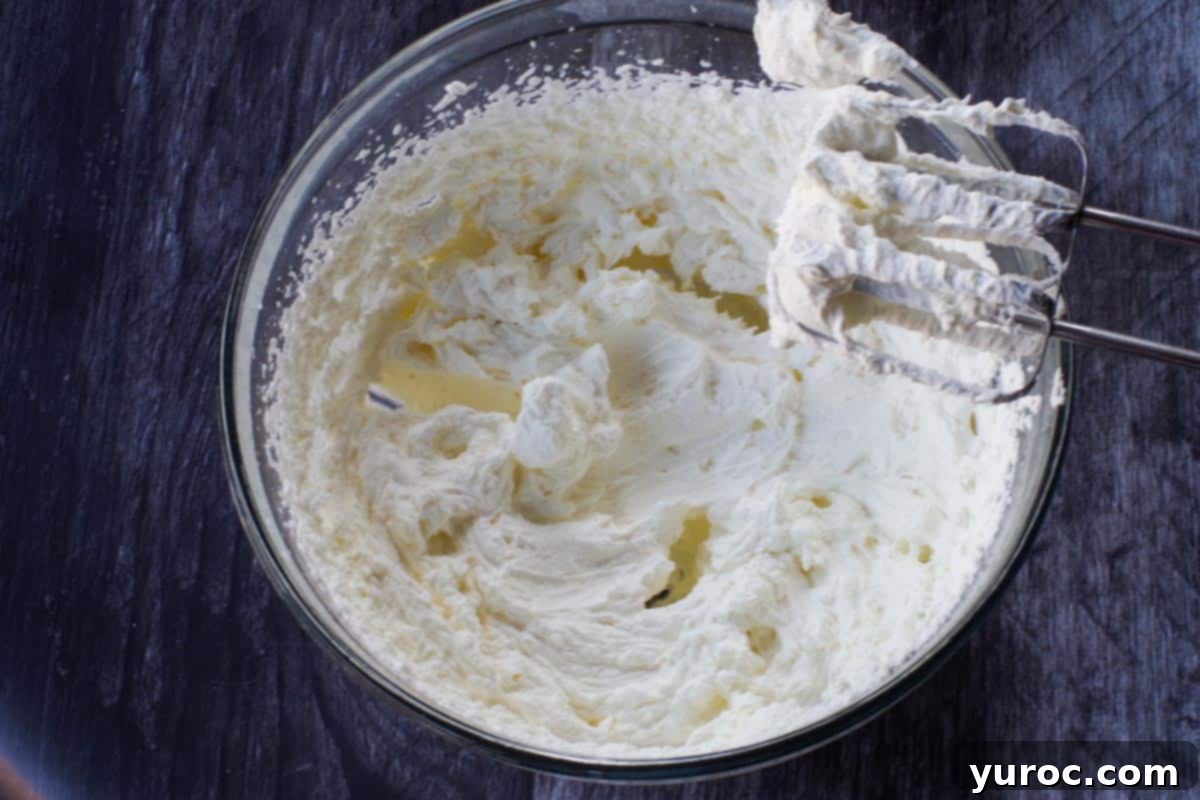 Effortless Pumpkin Perfection 12 A glass bowl filled with perfectly beaten whipped cream, showcasing stiff peaks, with electric mixer beaters nearby.