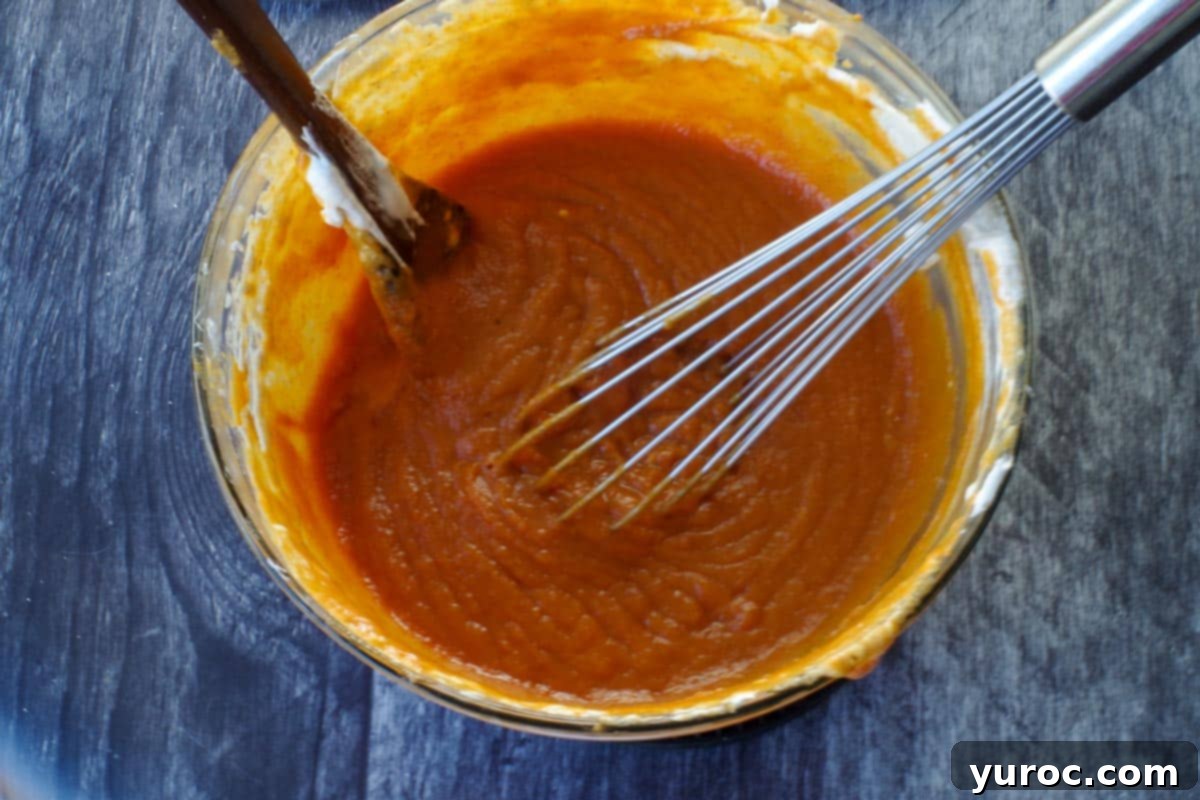 Effortless Pumpkin Perfection 7 A vibrant orange pumpkin mixture in a glass bowl, with a whisk and wooden spoon, showcasing its smooth texture.