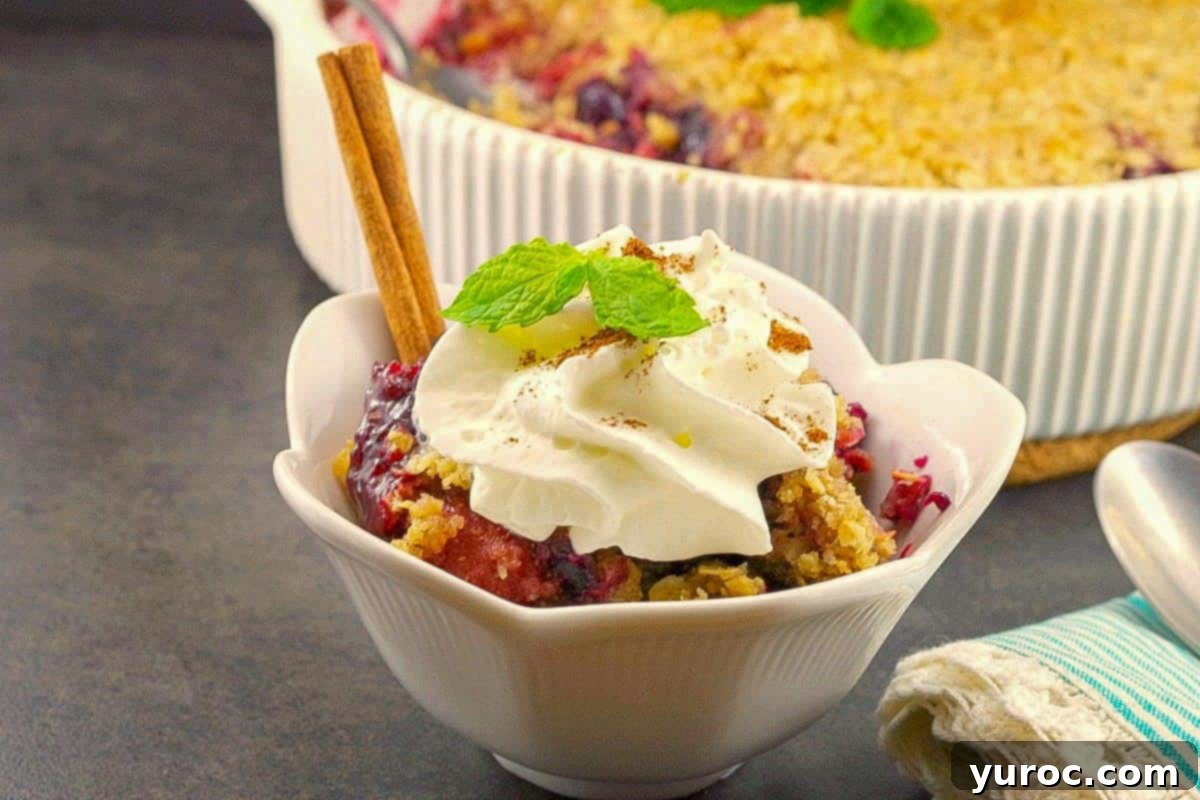 Triple Berry Crisp with frozen berries in a bowl with whipped cream and a dish of more in the background.